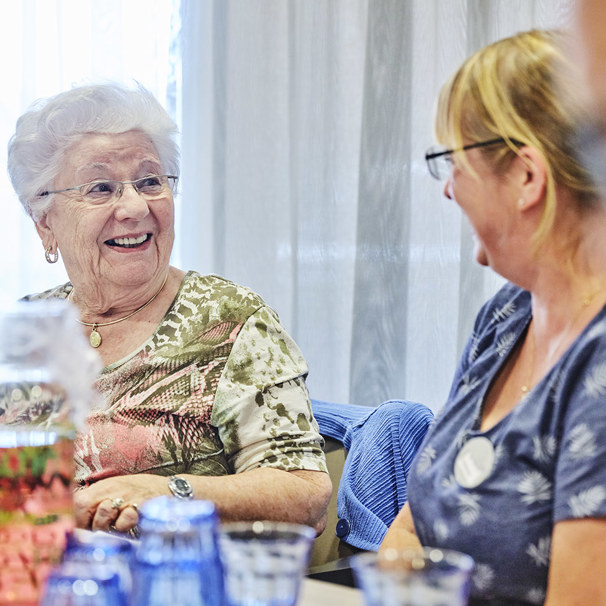 Twee dames lachend met elkaar in gesprek aan tafel, met daarop glazen met drinken